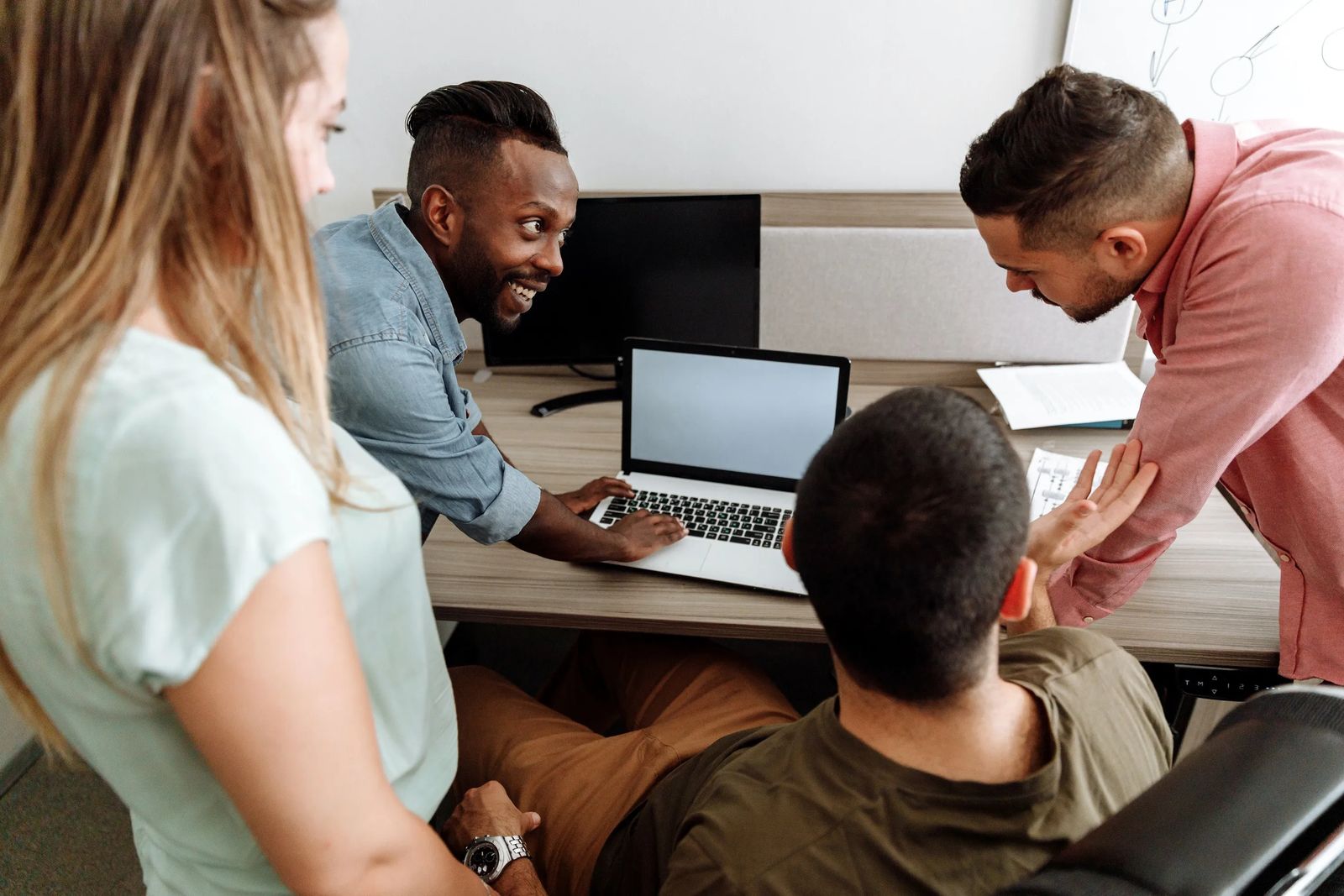 Four people looking over a laptop working together.