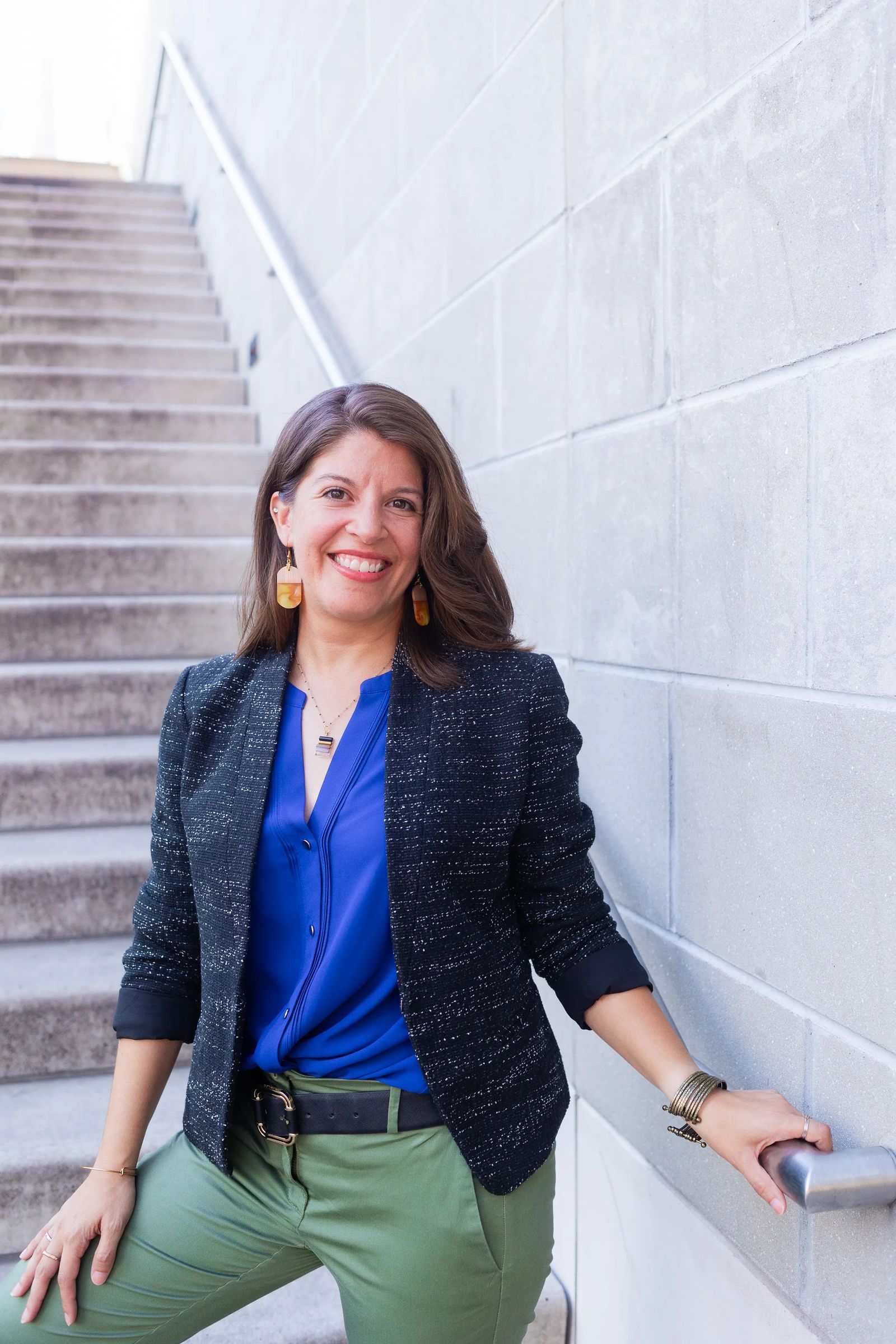 Fair skinned latina wear a black blazer and blue top standing on a concrete staircase